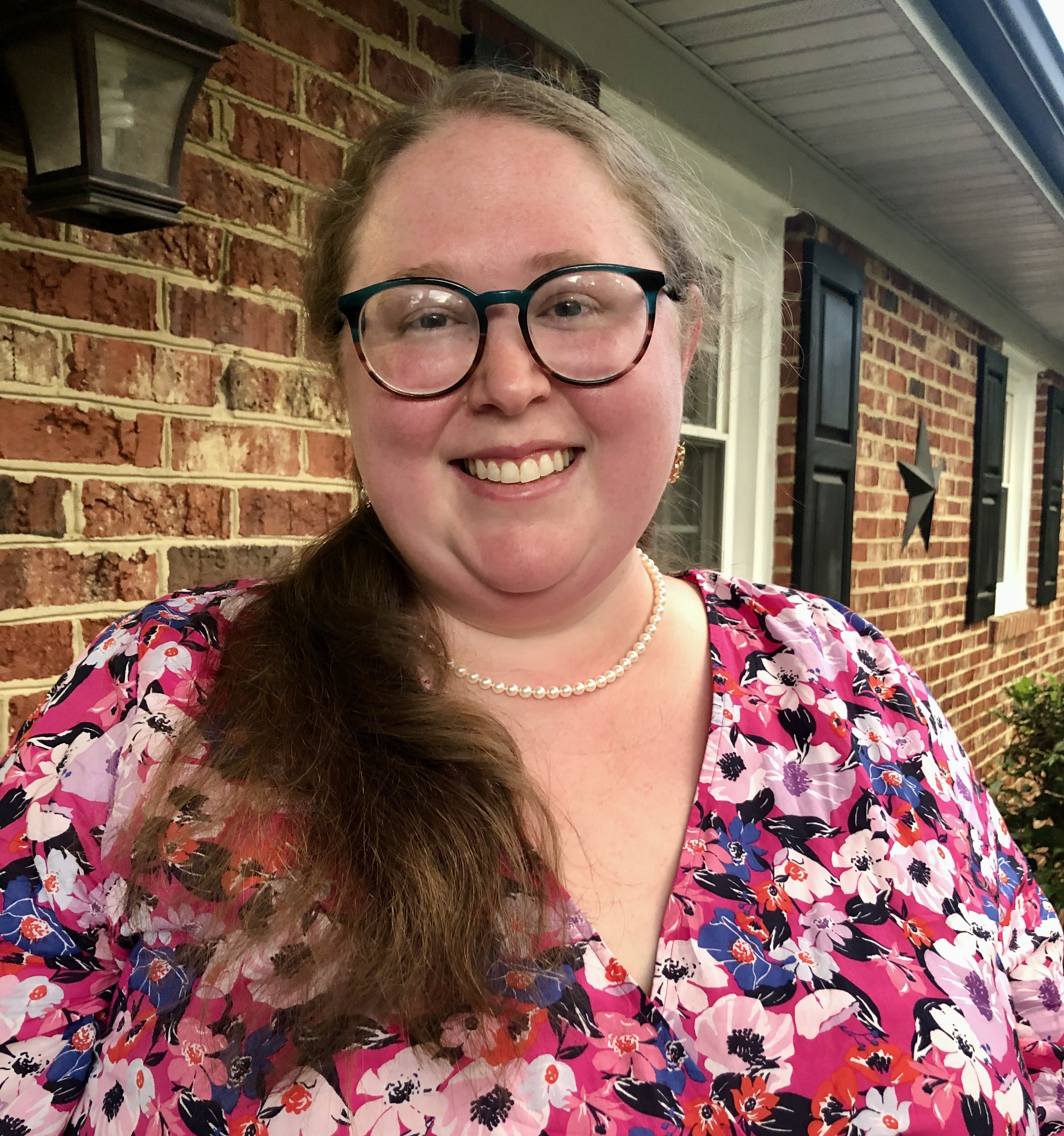 Melissa Allen wearing a pink blouse in front of a brick wall