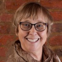 A woman wearing a dark brown turtle neck with black-rimmed glasses
