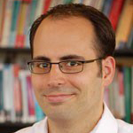 A man wearing a white button-up shirt with thin-rimmed glasses