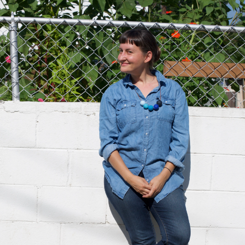 A woman wearing a blue denim top and jeans leaning against a cinderblock wall