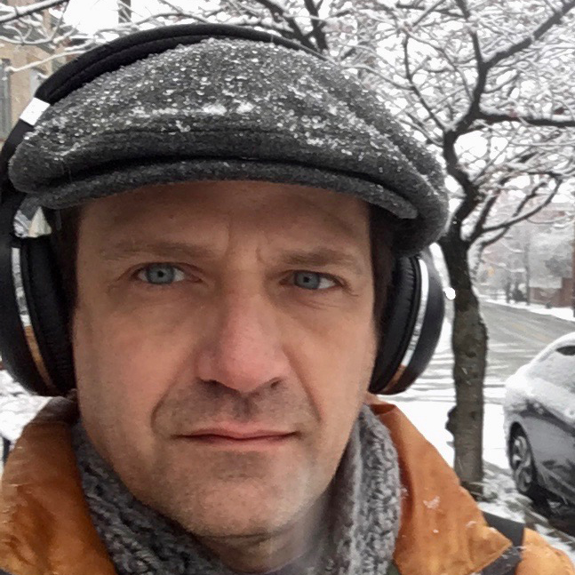 A man wearing a hat with a light brown jacket with a snowy background