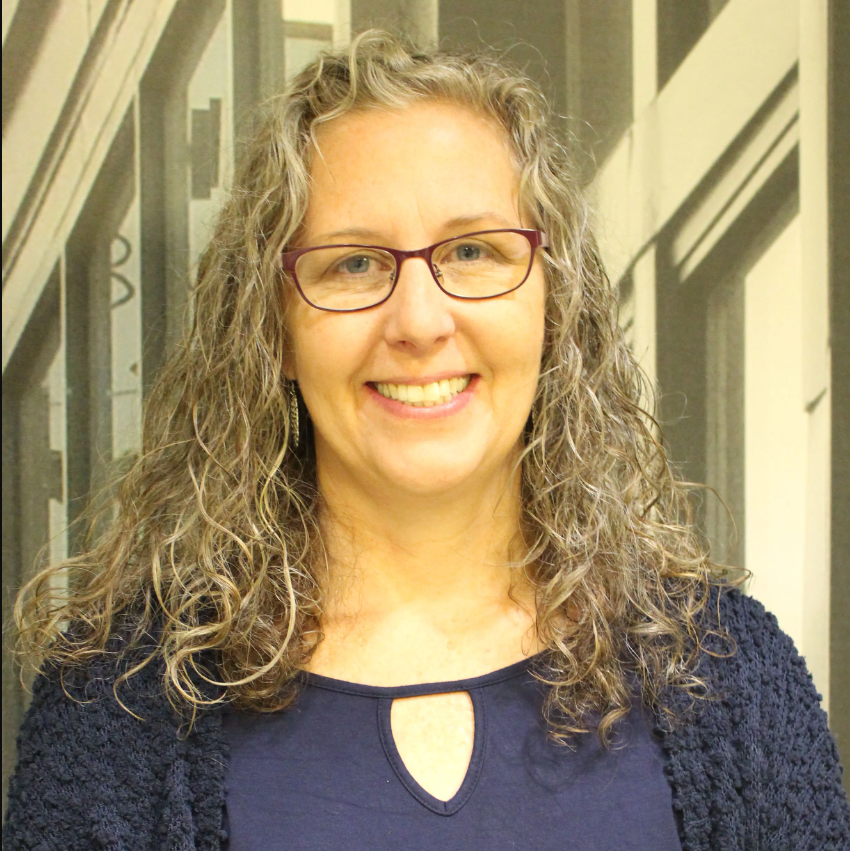 A woman with gray hair and glasses wearing a dark blue blouse and cardigan