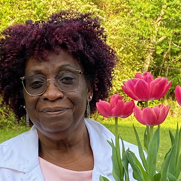 Ywonie Edwards Ingram wearing a light blue and pink shirts standing next to tulips.