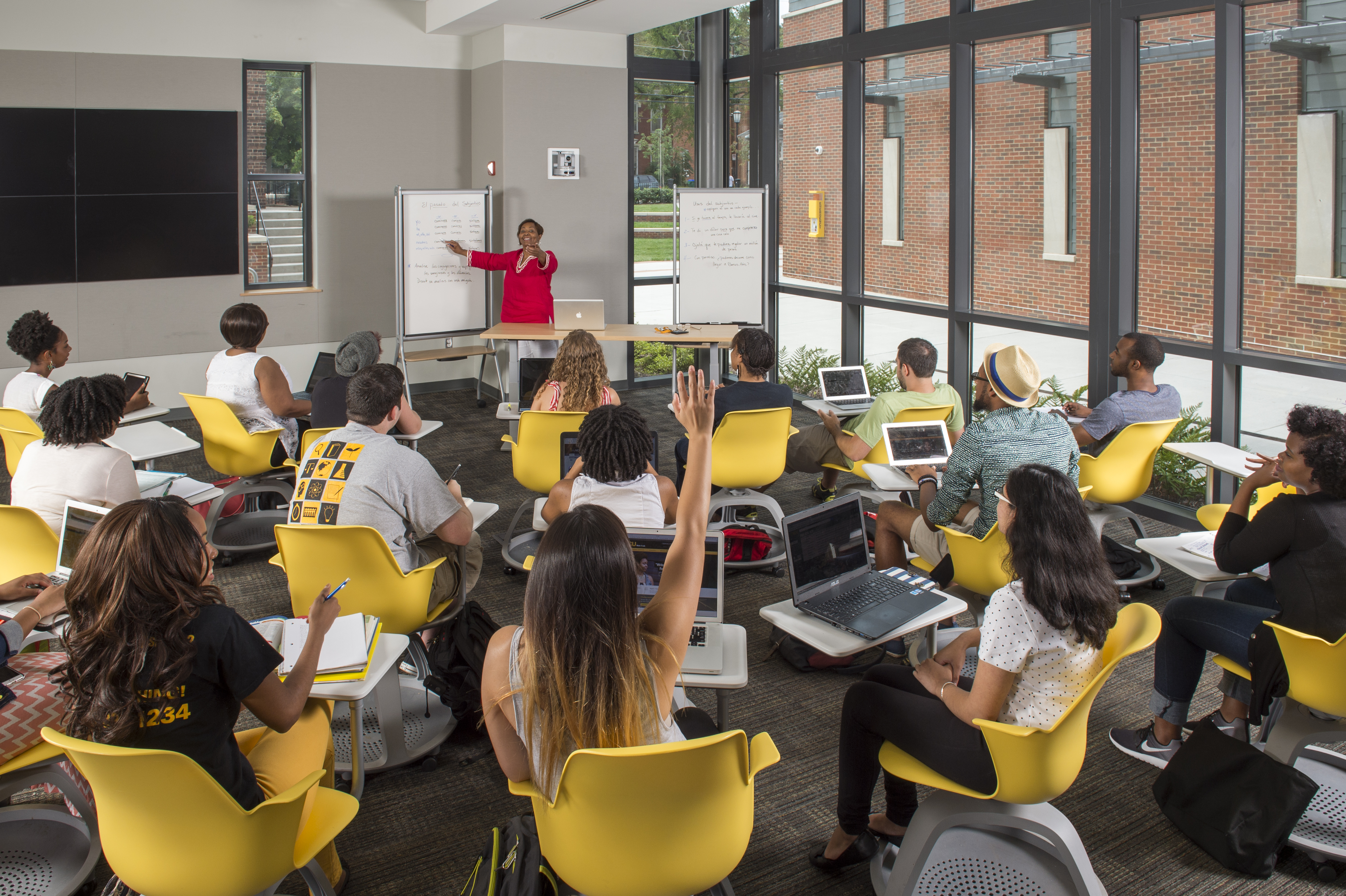 Students sit in a classroom with their hands raised